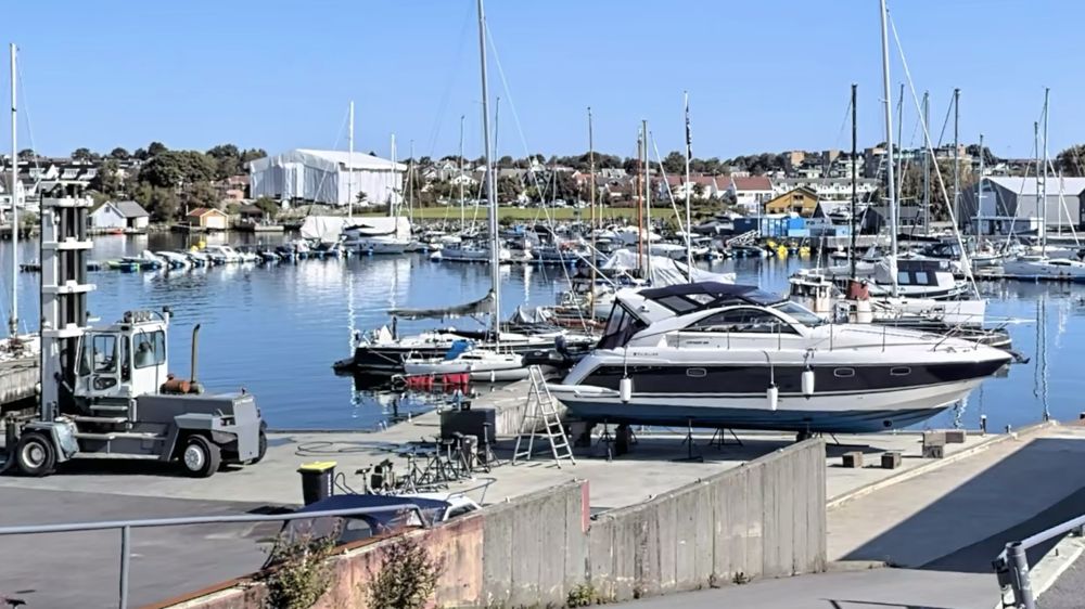 Motorbåt på land ved slippen, med truck og havnen i bakgrunnen.